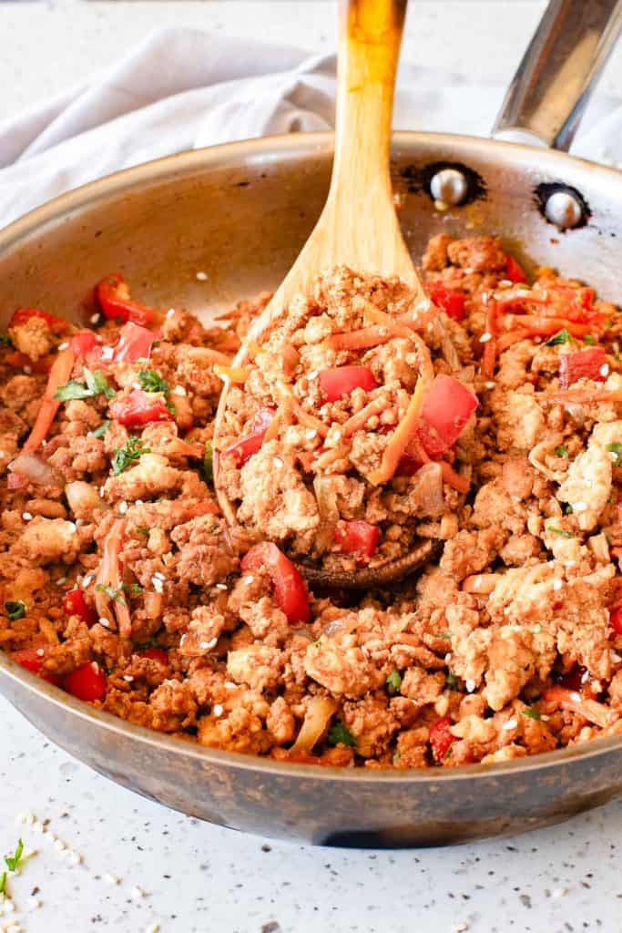 Ground turkey with diced tomatoes, onions, and herbs cooking in a skillet, stirred with a wooden spoon.