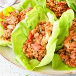 Leafy lettuce cups filled with seasoned ground meat and diced red bell peppers, arranged on a plate.