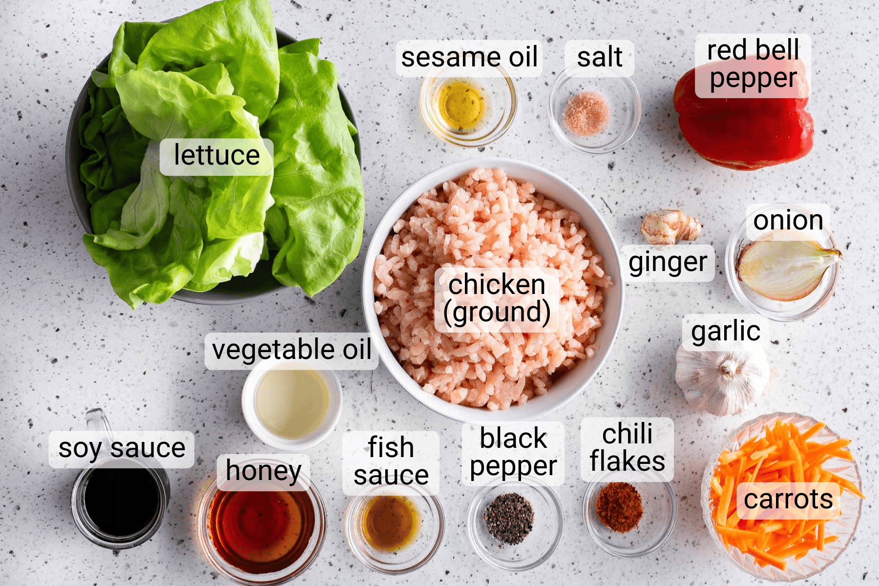 Assorted labeled ingredients for a chicken lettuce wrap recipe, including ground chicken, lettuce, sauces, oils, vegetables, and spices, arranged on a white countertop.