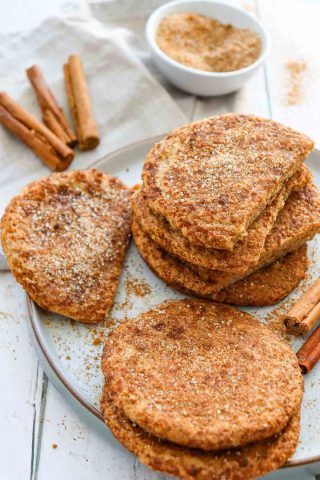 A plate of golden-brown flatbreads sprinkled with cinnamon sugar, with cinnamon sticks and a bowl of cinnamon sugar in the background.