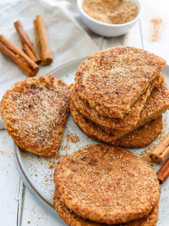 A plate of golden-brown flatbreads sprinkled with cinnamon sugar, with cinnamon sticks and a bowl of cinnamon sugar in the background.