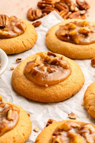 Close-up of several pecan caramel cookies on parchment paper, with chopped pecans scattered around.