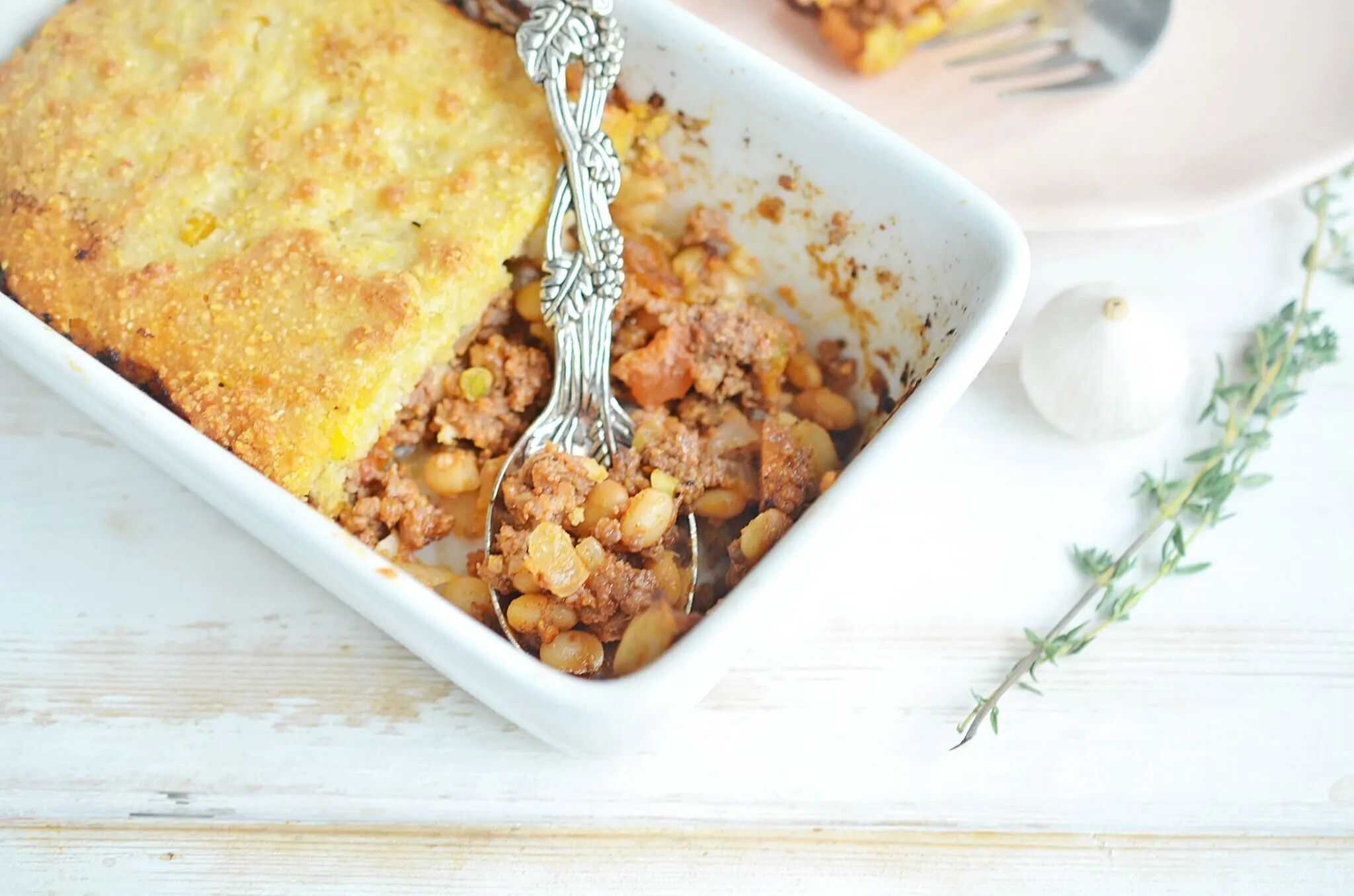 A white casserole dish with cornbread casserole and a silver serving spoon.