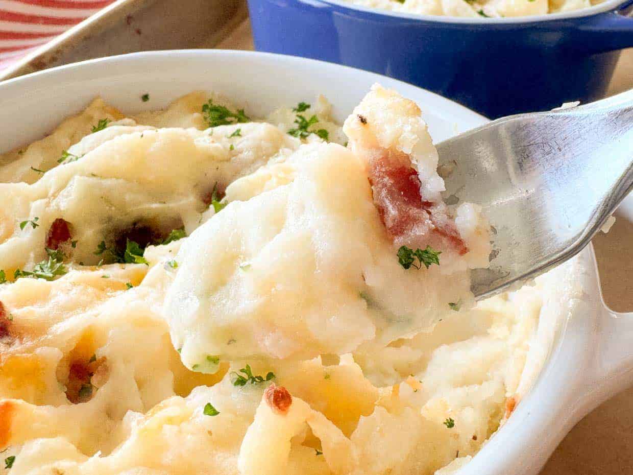 A close-up of a fork lifting a portion of mashed potatoes from a bowl.