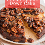 A pecan upside down cake with a slice removed, topped with glazed pecans, sits on a plate with a fork and napkin beside it.