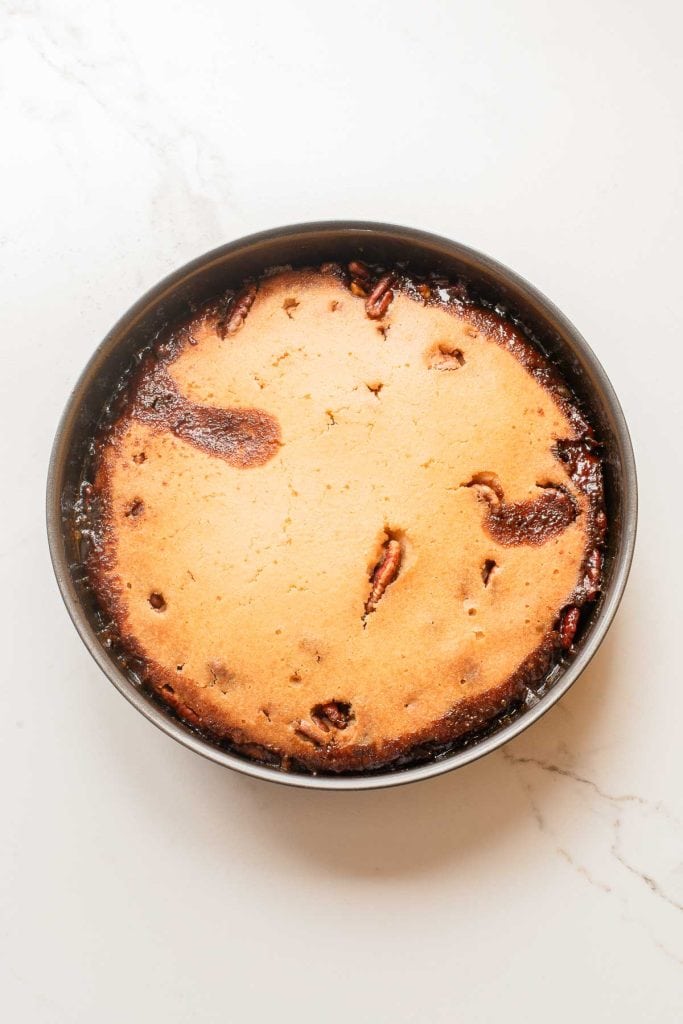 A round, baked pie with a golden-brown crust sits in a metal pan on a white, marbled surface.