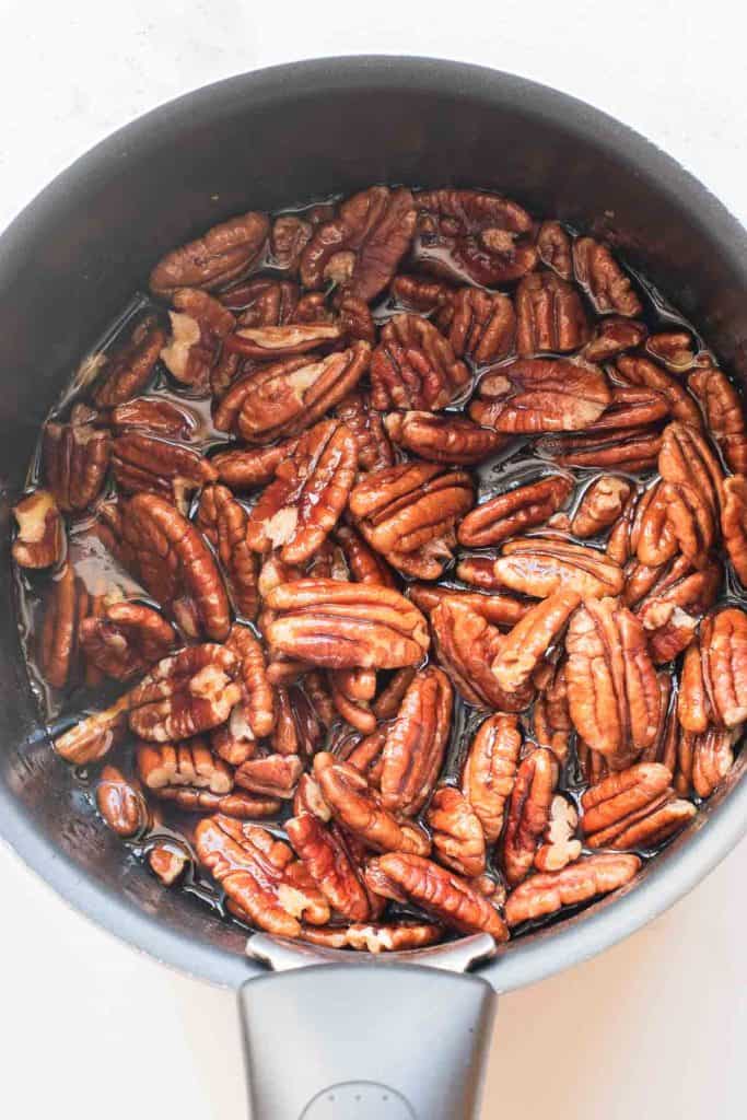 Pecan halves simmering in a saucepan with liquid, possibly being candied or prepared for a recipe.