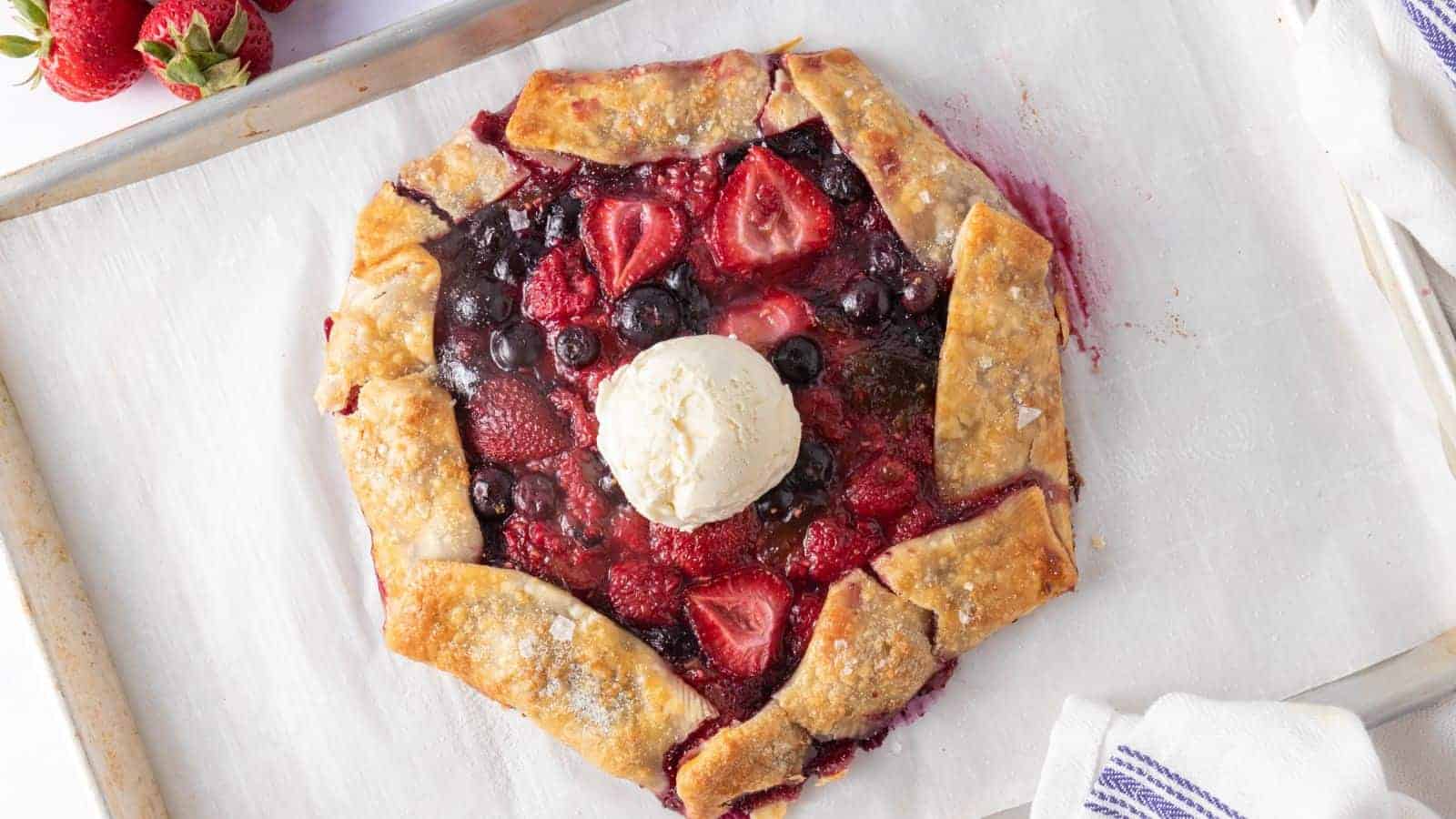 A mixed berry galette with a scoop of vanilla ice cream on top, placed on a parchment-lined baking sheet.