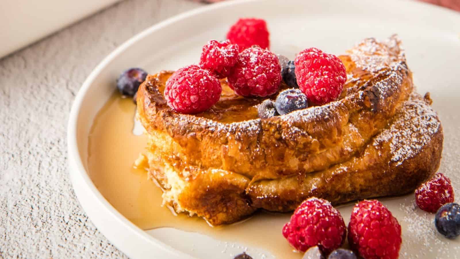 A plate of French toast topped with raspberries, blueberries, powdered sugar, and syrup.