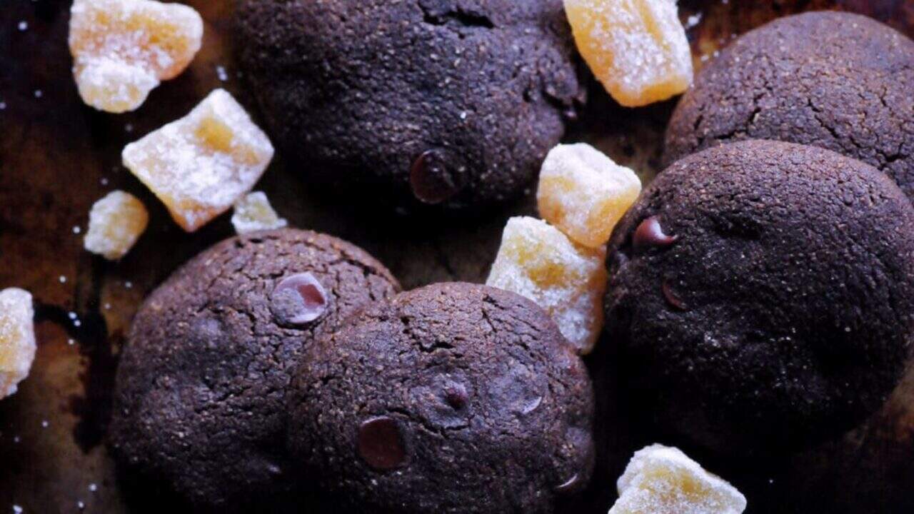 Five chocolate cookies and several pieces of crystallized ginger are arranged on a dark surface.