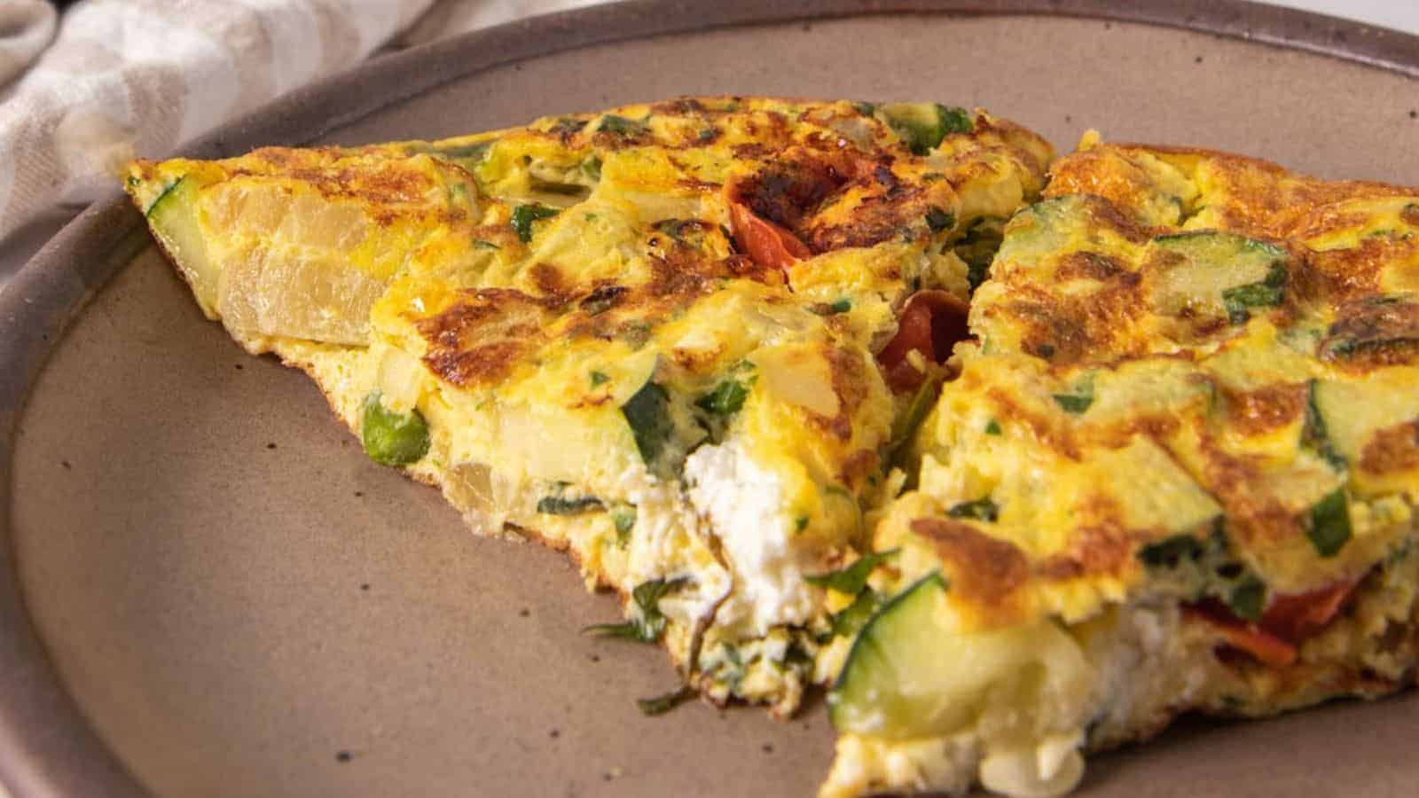 A close-up of two slices of vegetable frittata with visible pieces of zucchini, tomato, and cheese on a round ceramic plate.