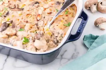 A baked casserole with pieces of chicken, mushrooms, and sliced almonds in a creamy sauce, served in a blue rectangular dish with a spoon.