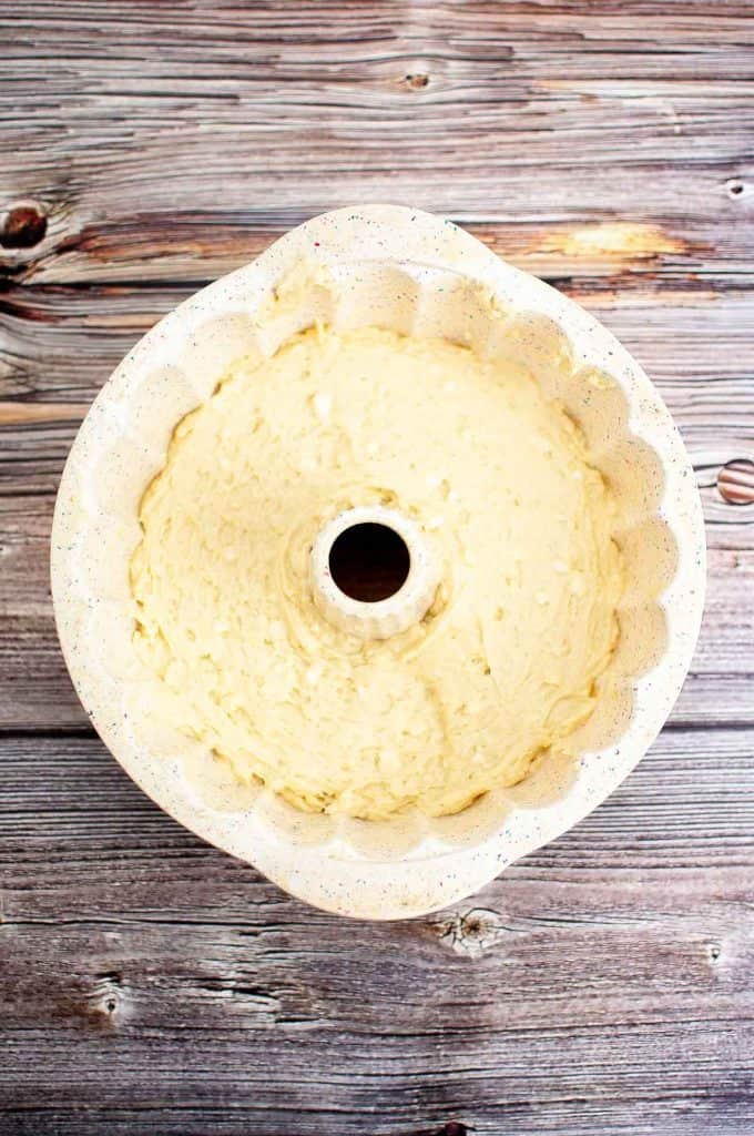 A Bundt cake pan filled with unbaked cake batter sits on a wooden surface.
