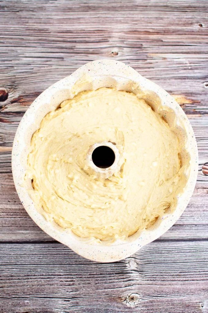 A bundt pan filled with unbaked cake batter sits on a wooden surface.