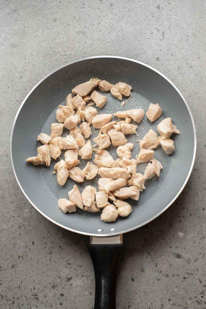 A frying pan with evenly cooked, diced pieces of chicken breast on a gray countertop.