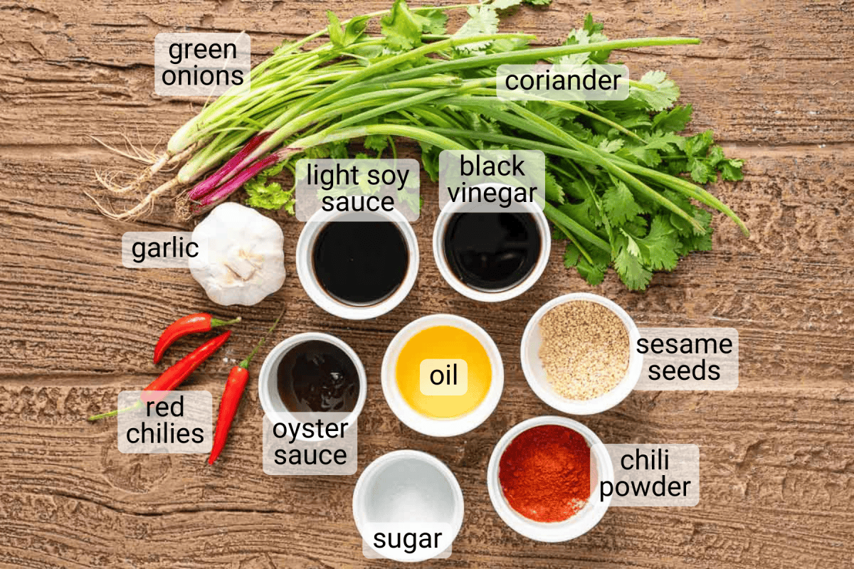 Various labeled ingredients including green onions, coriander, garlic, red chilies, soy sauce, black vinegar, oyster sauce, oil, sugar, sesame seeds, and chili powder on a wooden surface.