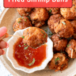 A plate of fried shrimp balls garnished with herbs, with one ball being dipped into a bowl of red sauce.