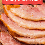 Close-up of several slices of honey glazed ham on a wooden surface with a sign above reading "Honey Glazed Ham.