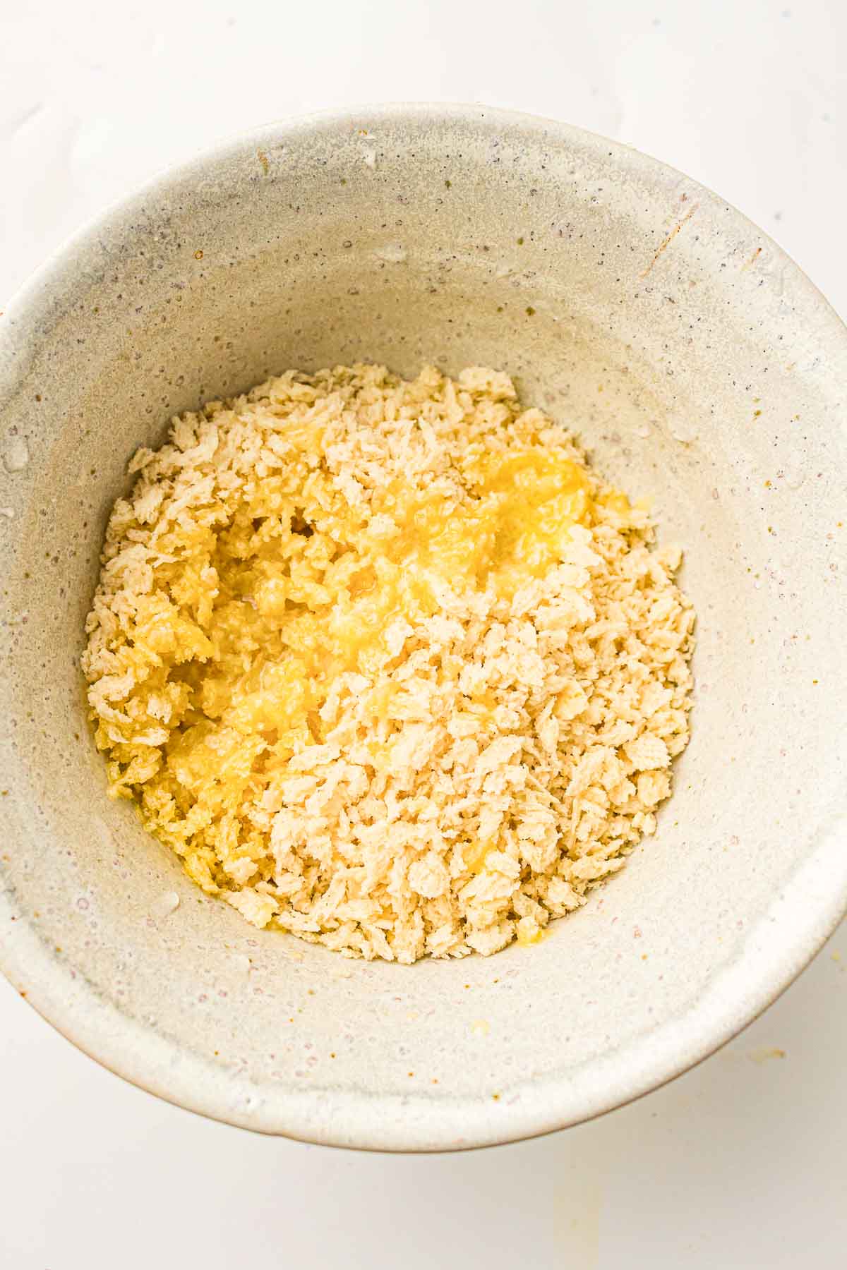 A ceramic bowl filled with breadcrumbs mixed with a liquid, possibly melted butter or oil, on a white surface.
