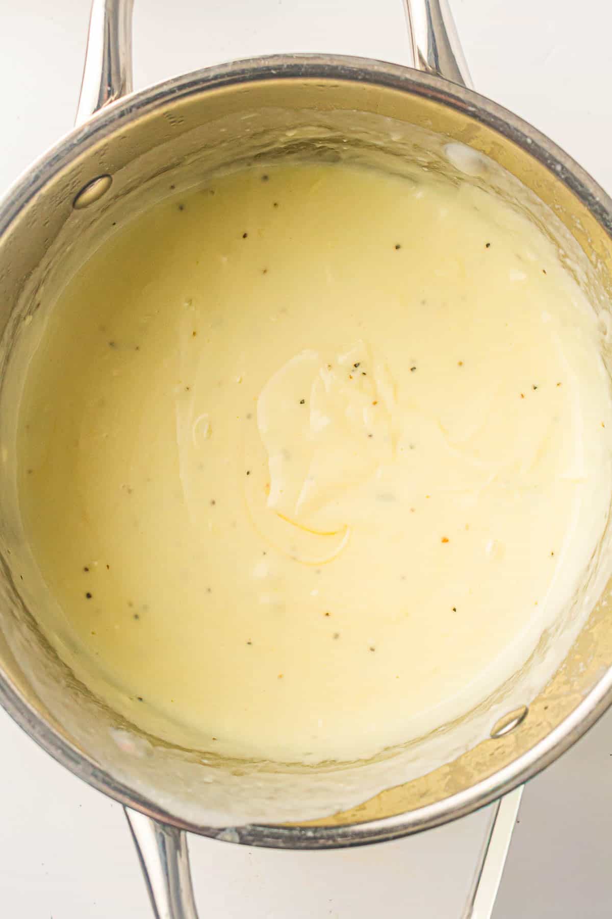 A stainless steel pot contains a creamy white sauce with visible black pepper specks, resting on a stovetop.