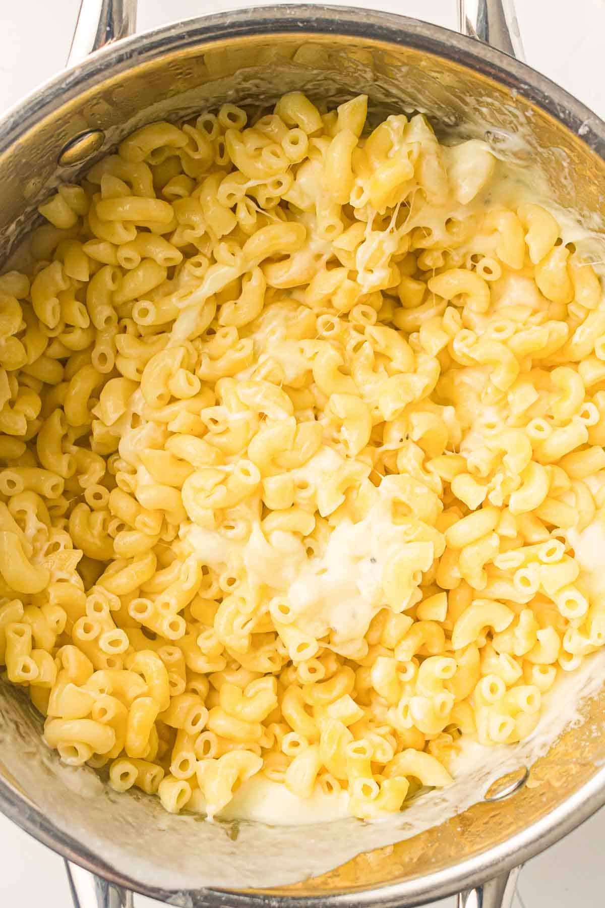 Cooked macaroni pasta mixed with melted cheese in a stainless steel pot, seen from above.