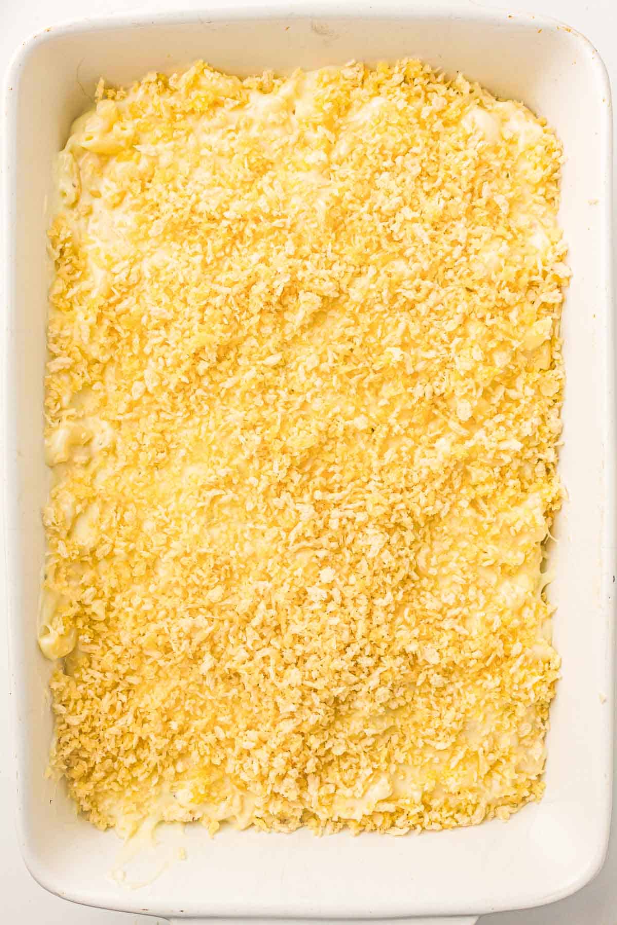 A baking dish filled with macaroni and cheese topped with a layer of shredded cheese and breadcrumbs, ready to be baked.