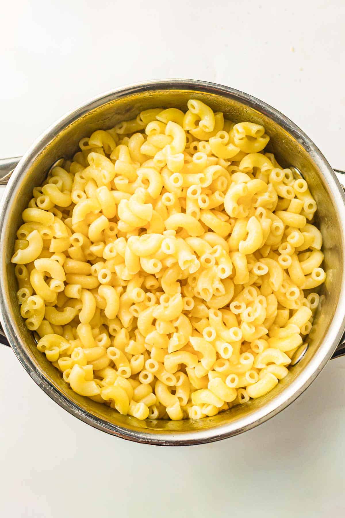 A stainless steel pot filled with cooked elbow macaroni pasta on a white background.