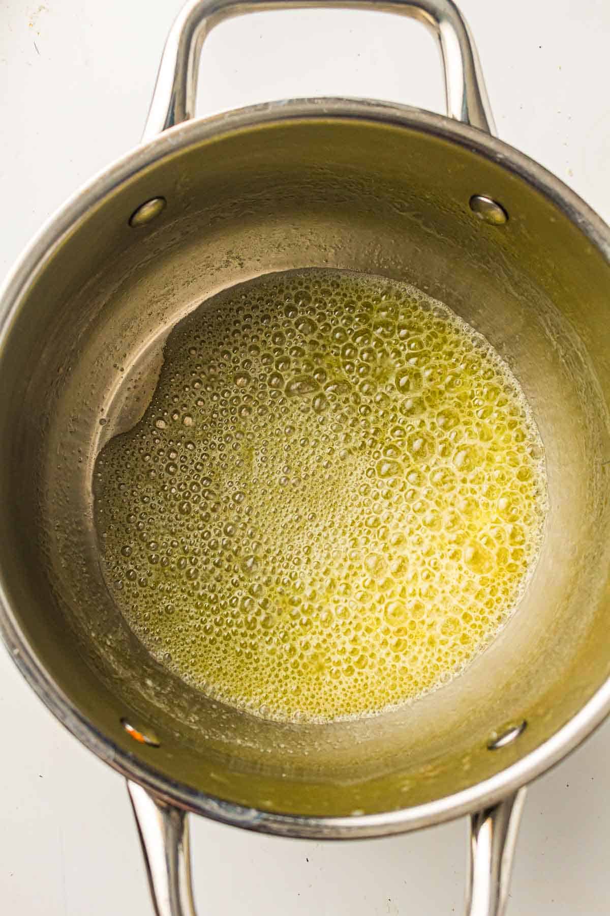 Melted butter bubbling in a stainless steel saucepan on a white surface.