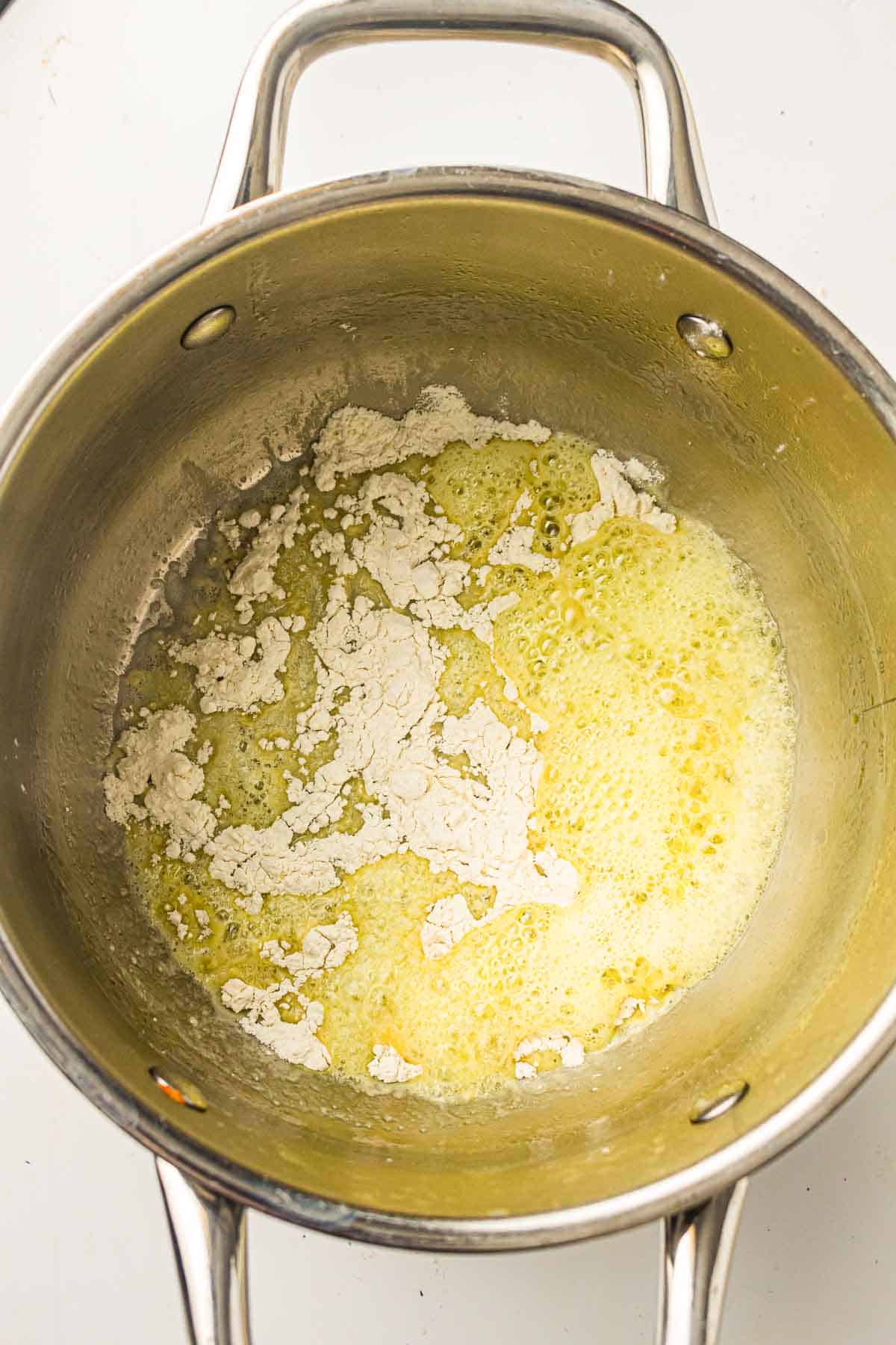 A stainless steel pot with melted butter and flour being mixed to make a roux.