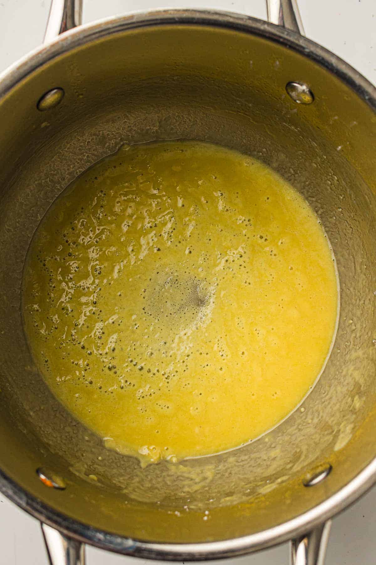 A saucepan containing a yellow, bubbling mixture, possibly a sauce or melted butter, seen from above.