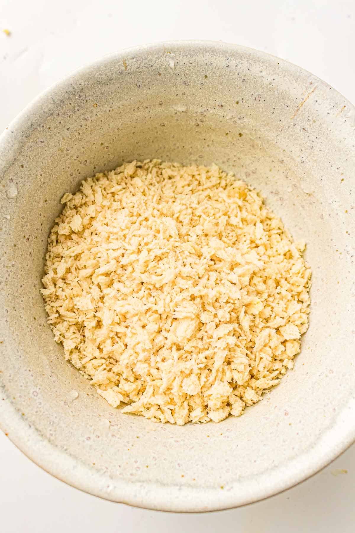 A ceramic bowl filled with light-colored panko breadcrumbs sits on a white surface.