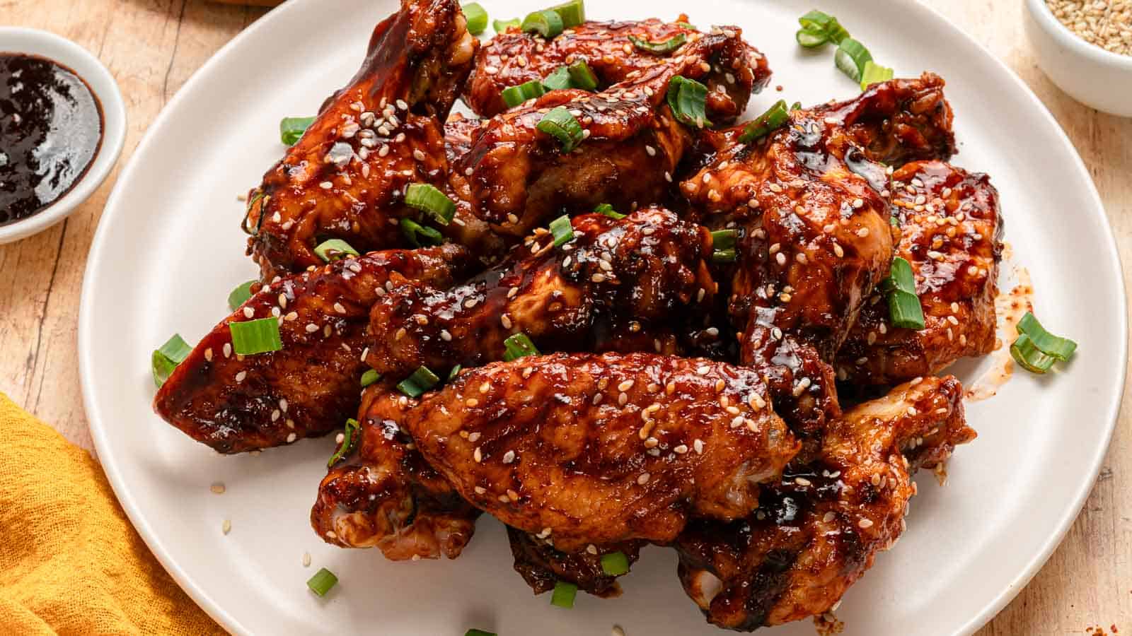 Plate of glazed chicken wings topped with sesame seeds and chopped green onions on a white dish.