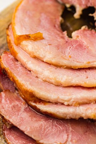 Several slices of cooked ham are arranged in a stack, showing their pink interior and slightly browned edges on a wooden surface.