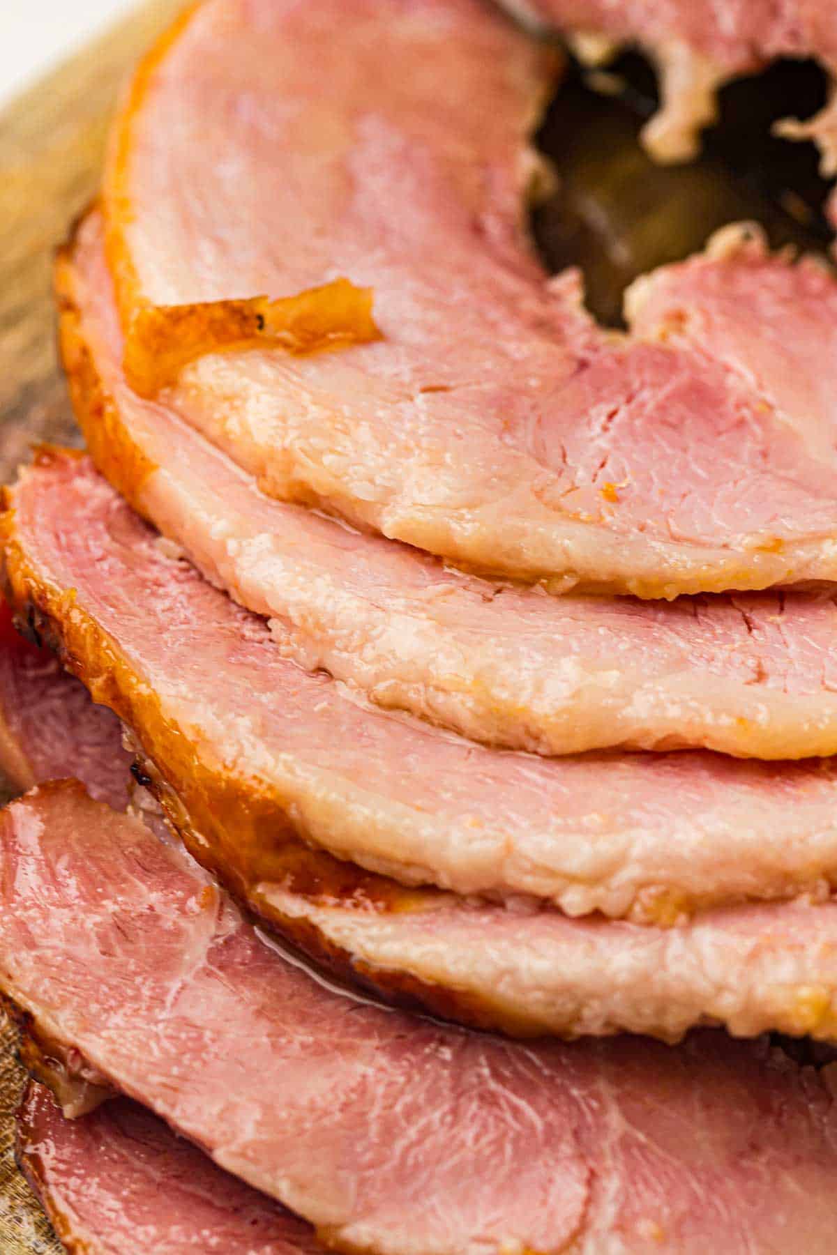 Several slices of cooked ham are arranged in a stack, showing their pink interior and slightly browned edges on a wooden surface.
