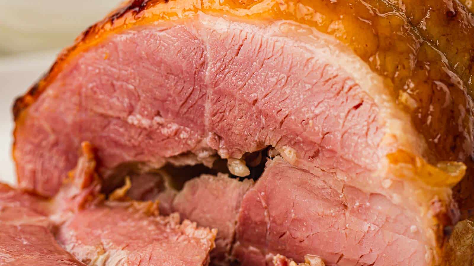Close-up of a juicy, glazed baked ham with a golden-brown crust and pink, tender interior, showing detailed texture and moistness.