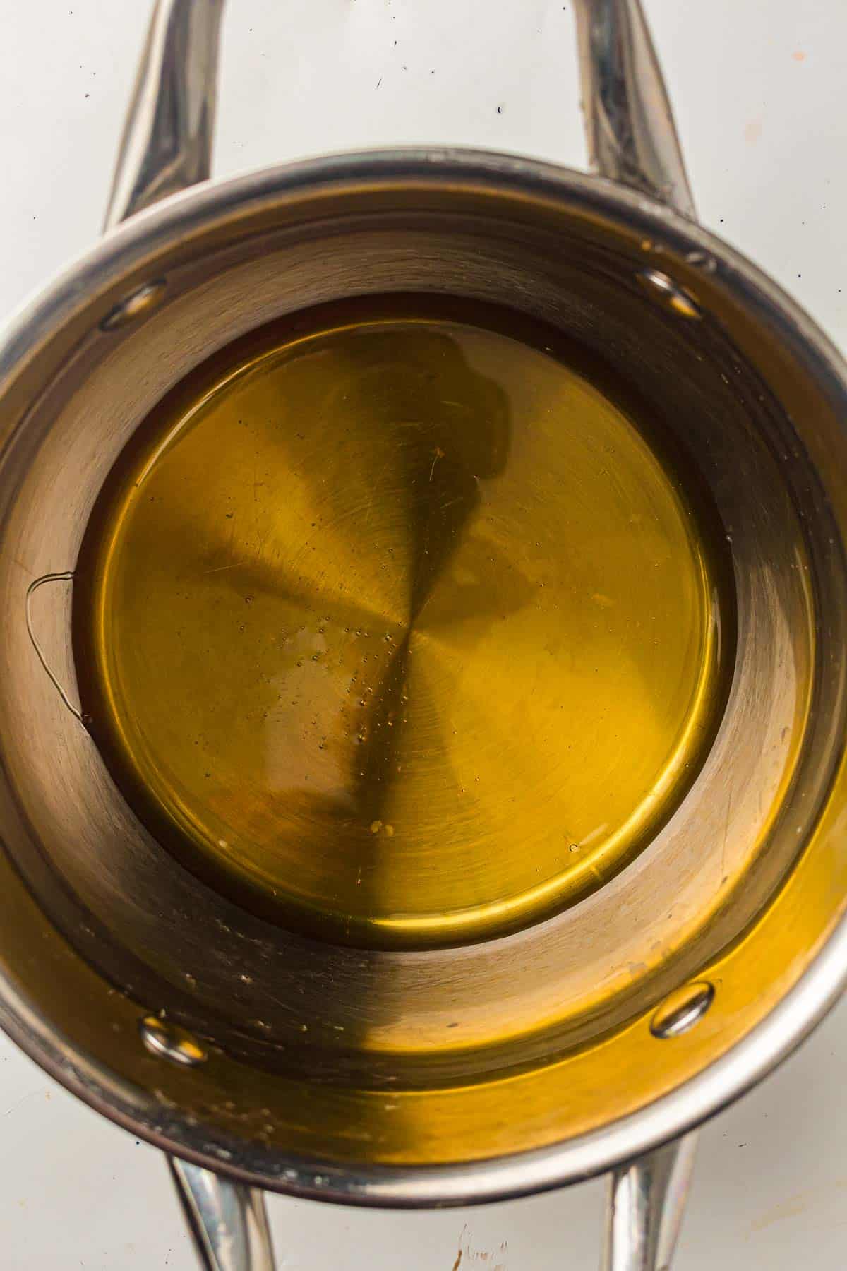A stainless steel pot filled with a layer of yellowish cooking oil, photographed from above.