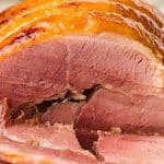 Close-up of a cooked, sliced ham showing its pink interior and glazed, browned outer layer.