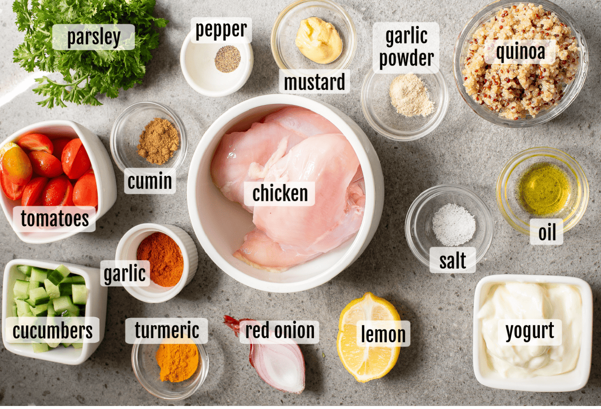 Assorted ingredients including raw chicken breast, tomatoes, cucumbers, red onion, lemon, yogurt, quinoa, spices, oil, and parsley arranged on a countertop.