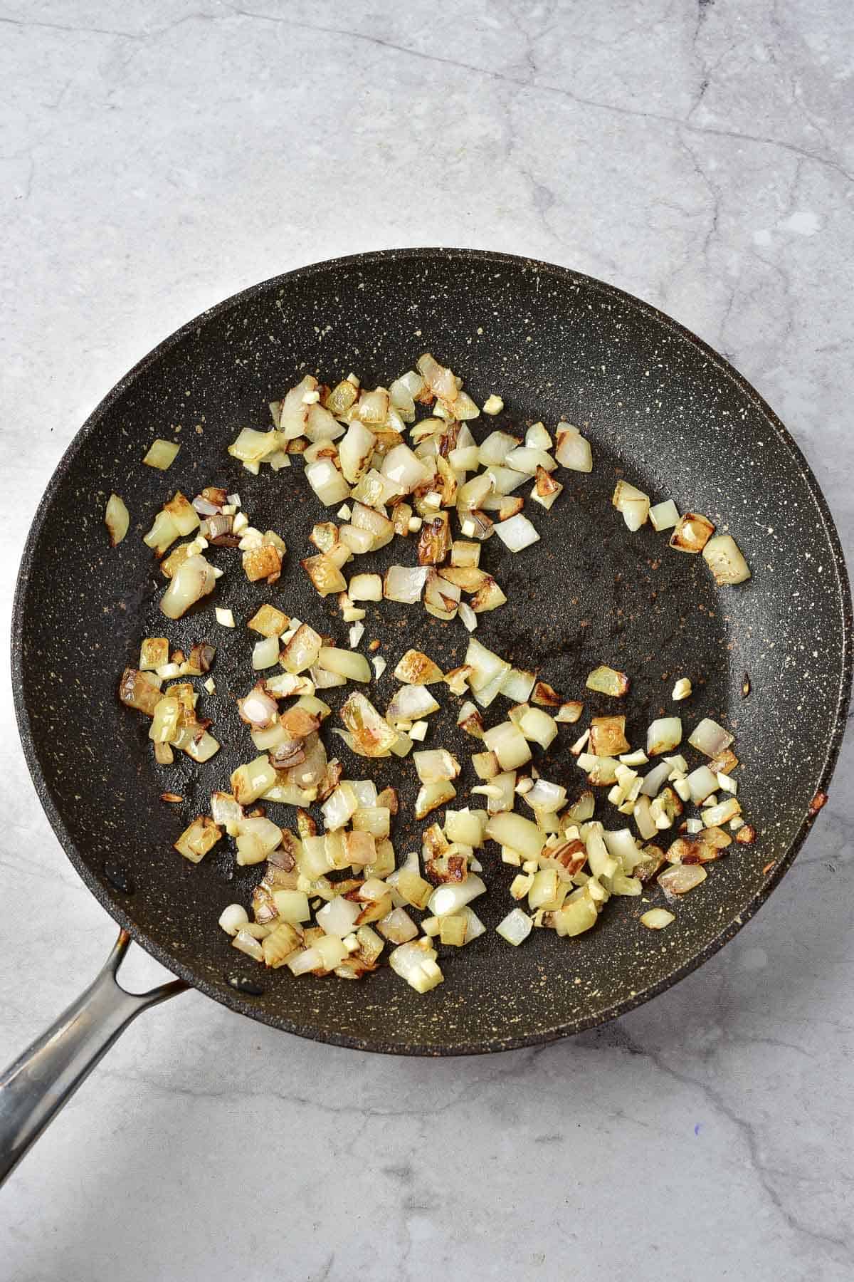 Chopped onions being sautéed and lightly browned in a nonstick frying pan on a light-colored countertop.
