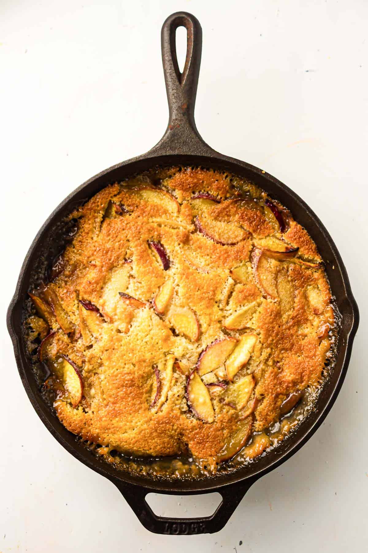 A baked fruit cobbler with a golden-brown crust and visible fruit slices in a black cast iron skillet on a white background.