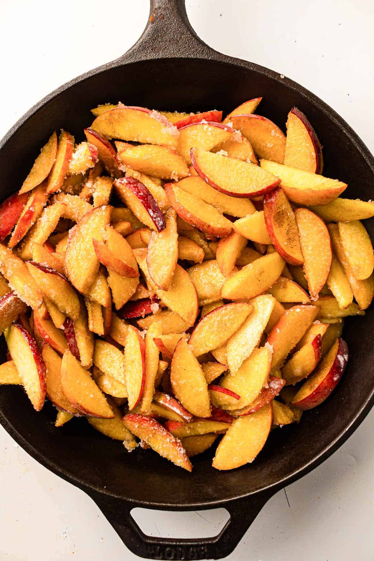Sliced peaches coated with sugar in a cast iron skillet.