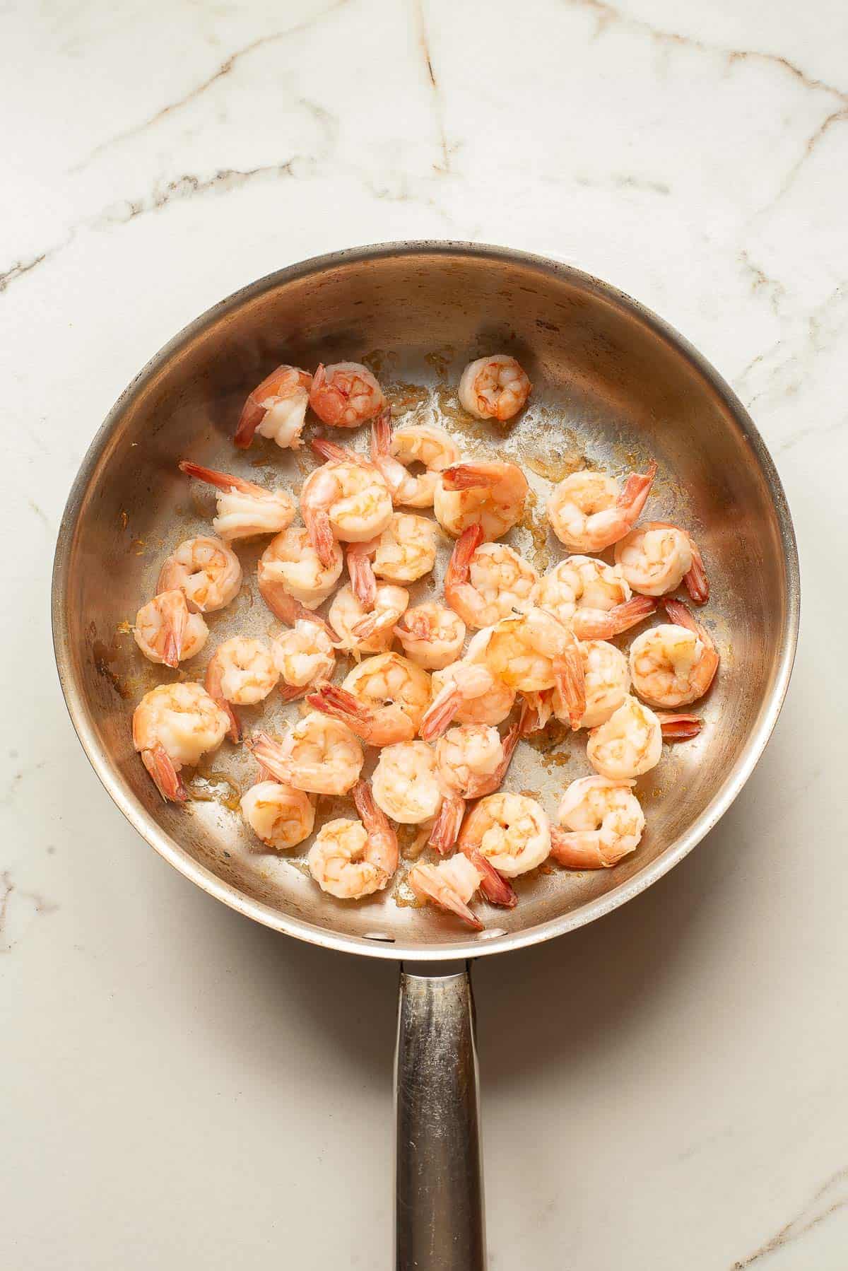 Cooked shrimp in a stainless steel skillet on a white marble countertop.