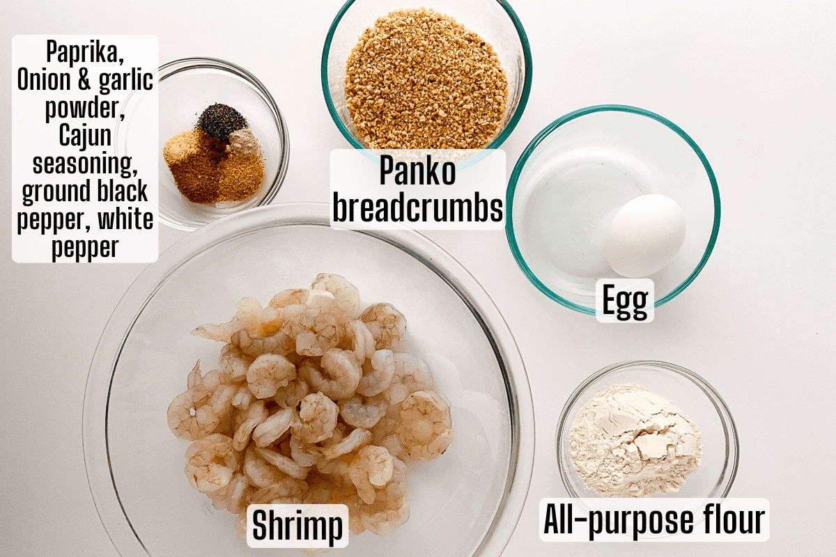 Bowls containing shrimp, panko breadcrumbs, an egg, all-purpose flour, and a mix of spices including paprika, onion and garlic powder, Cajun seasoning, black pepper, and white pepper.