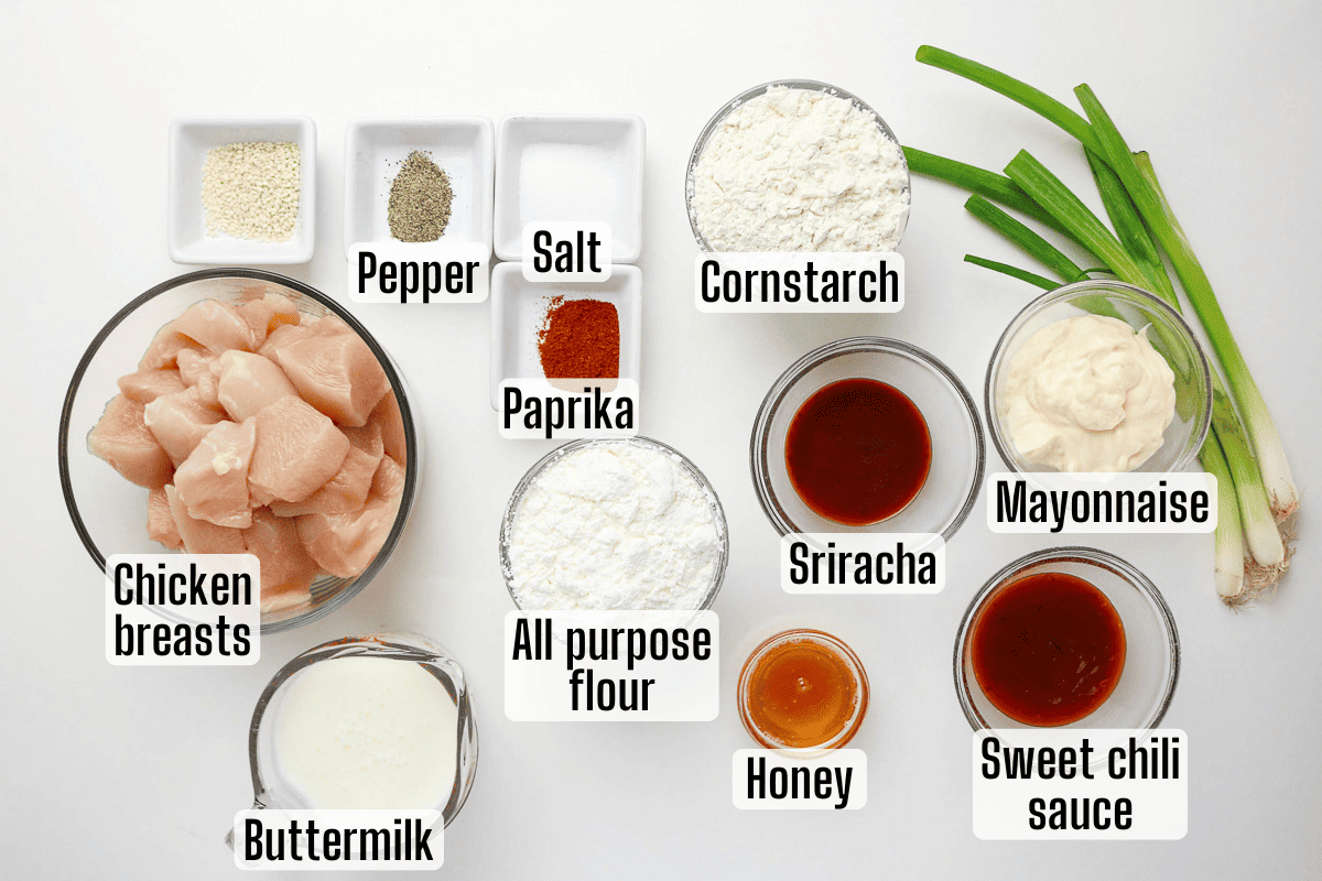 Labeled ingredients for a recipe, including chicken breasts, buttermilk, flour, cornstarch, mayonnaise, sriracha, honey, sweet chili sauce, paprika, salt, pepper, and green onions.