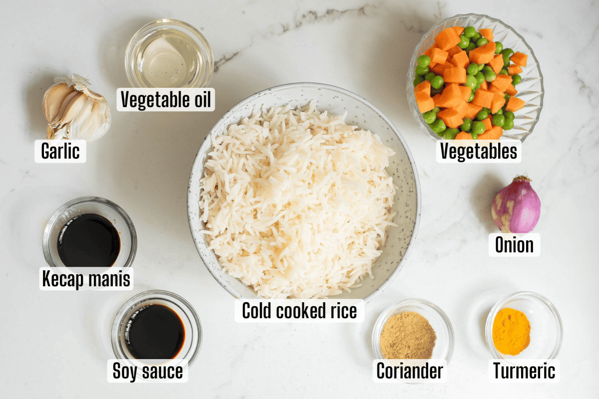 A bowl of cold cooked rice surrounded by labeled ingredients: vegetable oil, garlic, kecap manis, soy sauce, vegetables, onion, coriander, and turmeric on a white background.