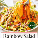 A colorful plate of mixed vegetable salad with peanut dressing, topped with sesame seeds, next to a fork and a small bowl of dressing. Text reads “Rainbow Salad with Peanut Dressing.”.