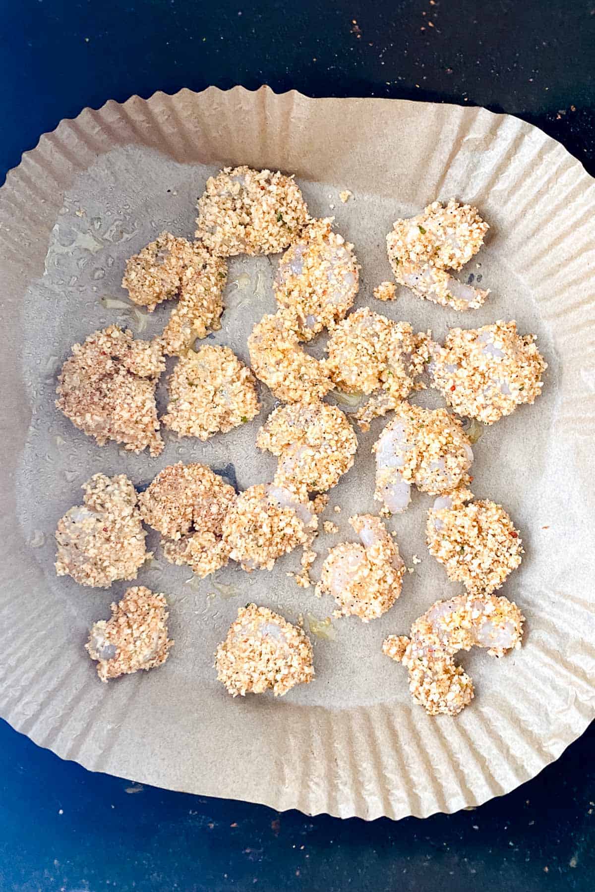 Uncooked breaded shrimp arranged on a piece of parchment paper inside a round baking pan.