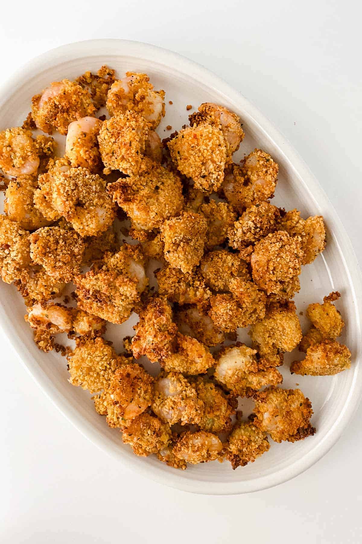 Oval white plate filled with breaded, baked shrimp arranged in a single layer on a white surface.