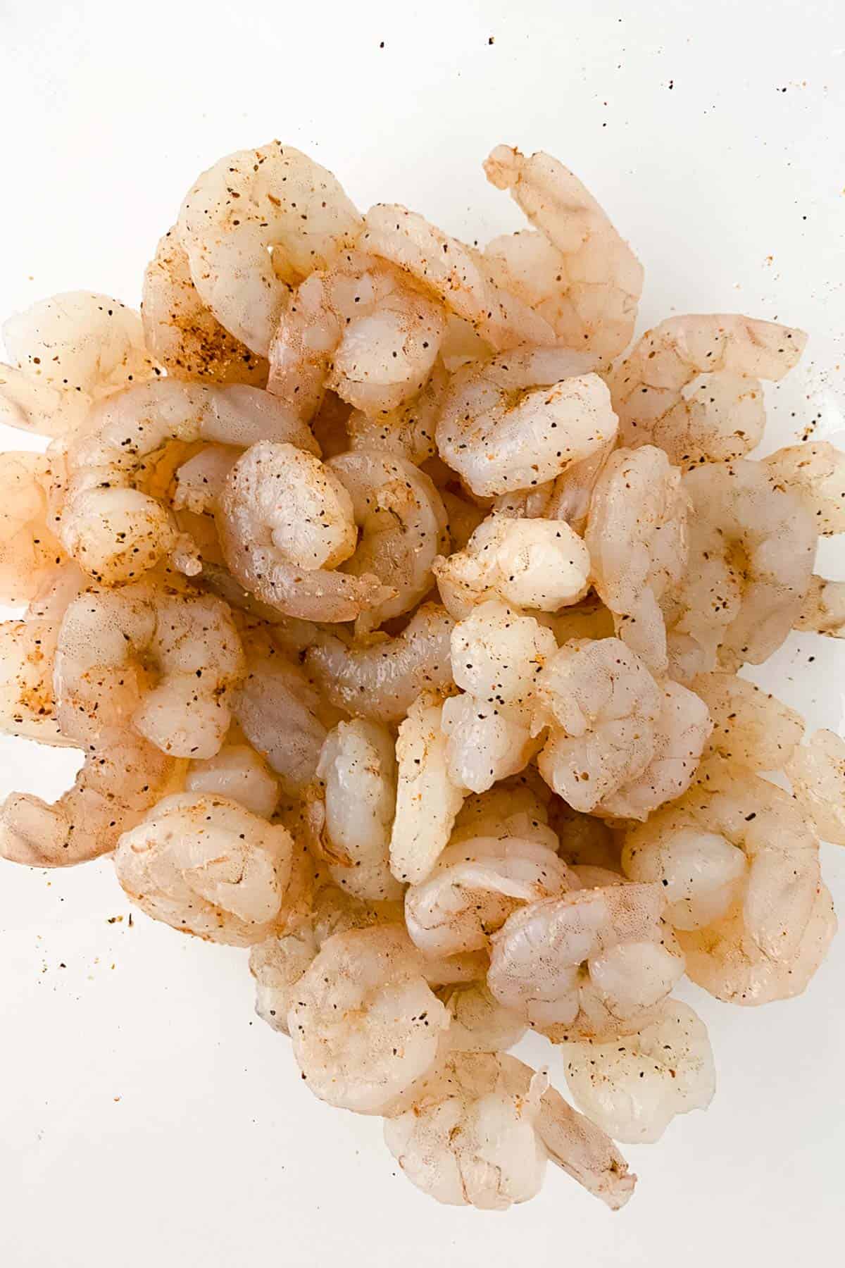 Raw, peeled shrimp seasoned with spices, piled on a white surface.