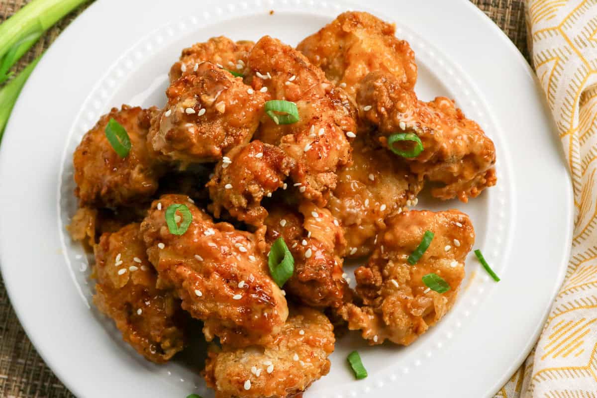 Fried chicken pieces topped with sesame seeds and chopped green onions are arranged on a white plate.